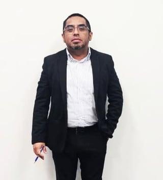 Man wearing black blazer and light striped shirt standing against white background
